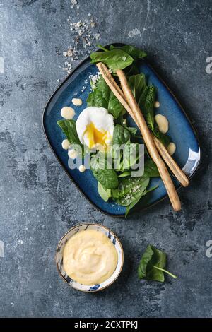 Oeuf poché sur épinards frais avec sauce hollandaise, de sel et de bâtonnets de pain servi dans un carré bleu sur la plaque texture background bleu. Vue d'en haut, Banque D'Images