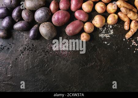 Variété de matières organiques non cuits pommes de différents types et couleurs rouge, jaune, violet avec différents de sel texture background sombre. Vue de dessus, co Banque D'Images