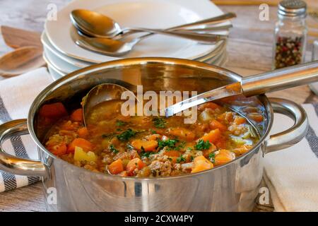 soupe de légumes avec viande hachée dans une casserole avec louche sur une table en bois Banque D'Images