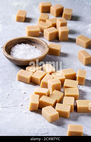 Bonbons fudge caramel salé servi sur planche de bois avec la fleur de sel à bol en bois gris sur fond de texture. Close up Banque D'Images