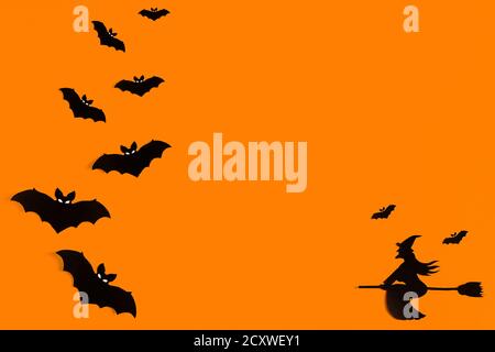 Silhouettes d'un troupeau de chauves-souris et d'une sorcière volant sur un balai en papier noir sur fond orange. Modèle de message d'accueil pour Halloween avec espace de copie Banque D'Images