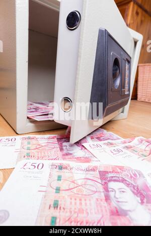 Coffre-fort domestique assis sur les planchers et débordant avec des billets de cinquante livres britanniques. Banque D'Images