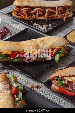 Des sandwiches de baguette aux ingrédients variés servis dans des assiettes en céramique sur une table en bois. Image isolée. Variété de sandwichs Banque D'Images