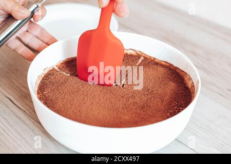 Délicieux gâteau au tiramisu avec crème et cacao sur le plateau. La main des femmes coupe le gâteau Banque D'Images