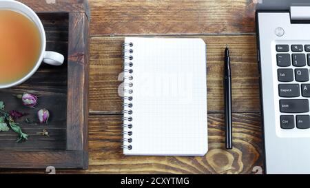 Plateau en bois avec une tasse de tisane, un ordinateur portable et un carnet ouvert et un stylo noir sur une table en bois sombre, le concept de travail de la maison, télécommande WO Banque D'Images