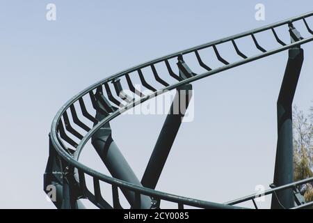 Montagnes russes incurvées dans un parc à thème ou d'attractions, pistes métalliques vertes vides et fond bleu ciel. Banque D'Images