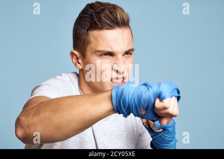 homme sportif en gants de boxe bleus et t-shirt en bleu vue rognée des poinçons d'entraînement en arrière-plan Banque D'Images