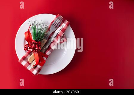 Assiette blanche, fourchette, couteau et décoration de Noël sur fond rouge Banque D'Images