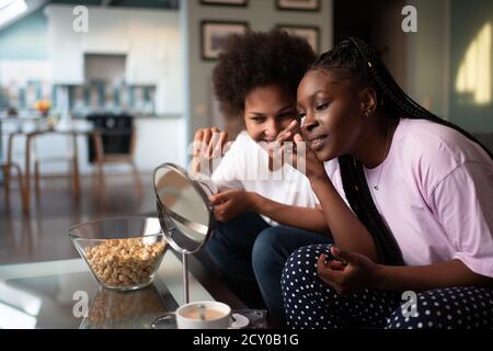 Amies multiethniques avec sous les yeux souriant et regardant miroir à la maison Banque D'Images