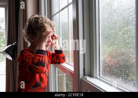 Jeune garçon regarde à travers la fenêtre couverte par la pluie avec des jumelles prétendant Banque D'Images