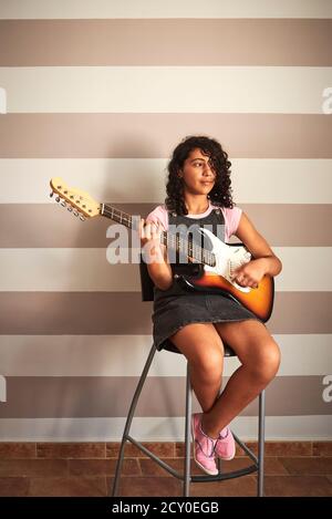 une petite fille avec des cheveux bouclés apprenant à jouer de la guitare. Concept de musique Banque D'Images