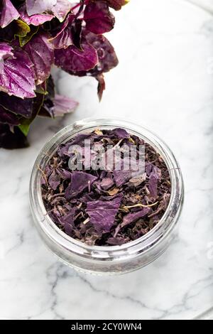 Feuilles de basilic violets séchées dans un bol avec feuilles fraîches sur un plateau de pierre. Mise au point sélective. Banque D'Images