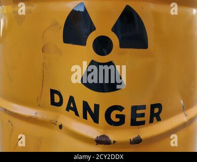 Panneau de danger noir sur cylindre en métal rouillé peint en jaune avec surface endommagée grondée Banque D'Images