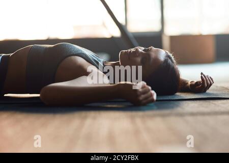 Femme de fitness épuisée dans des vêtements de sport couché sur le sol à la salle de gym, gardant les yeux fermés et se reposant après l'entraînement, prenant une pause pendant l'entraînement. Sport, bien-être et mode de vie sain Banque D'Images