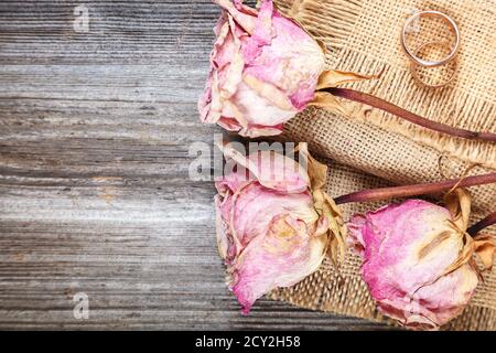 Anneaux de mariage et roses fleurs séchées sur fond de bois. Banque D'Images