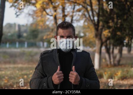 Un homme sous un manteau et un masque médical sur le fond d'un parc d'automne, le concept de la vague d'automne du coronavirus, Banque D'Images