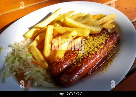 Currywurst allemand traditionnel, servi avec des frites sur une assiette blanche. Table en bois orange comme arrière-plan. Banque D'Images