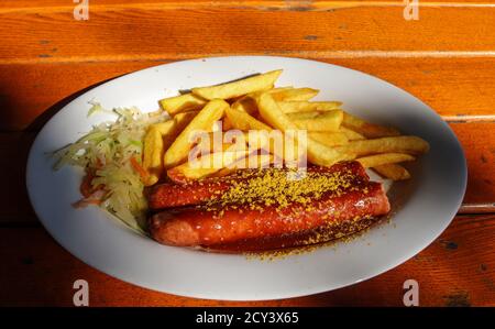 Currywurst allemand traditionnel, servi avec des frites sur une assiette blanche. Table en bois orange comme arrière-plan. Banque D'Images