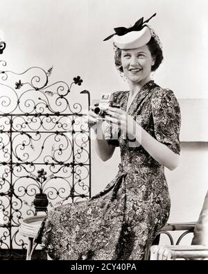 FEMME SOURIANTE DES ANNÉES 1940 PHOTOGRAPHE REGARDANT L'APPAREIL PHOTO TENANT UN REFLEX PORTER UNE ROBE IMPRIMÉE CHAPEAU SILLY ASSIS SUR LE PATIO EXTÉRIEUR - G1023 HAR001 HARS SILLY STYLE DE VISAGE PHOTOGRAPHE COMMUNICATION JOIE DE VIVRE CÉLÉBRATION FEMMES EMPLOIS PATIO MAISON VIE ASSIS ESPACE DE COPIE DEMI-LONGUEUR FEMMES PERSONNES INSPIRATION CARACTÈRE CONFIANCE EXPRESSIONS B&W PORTE DE CONTACT OCULAIRE VISION COMPÉTENCE PROFESSION BONHEUR COMPÉTENCES TÊTE ET ÉPAULES STYLES SOCIÉTÉ BUSYBODY SUR L'OPPORTUNITÉ OCCUPATIONS CONNEXION CONCEPTUEL STYLISÉ CRÉATIVITÉ MODES MOYEN-ADULTE FEMME MI-ADULTE RELAXATION SNOOD SNOOD TRAVAILLÉ NOIR ET BLANC Banque D'Images