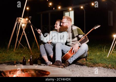 Couple caucasien heureux, femme brune et homme barbu avec guitare au pique-nique dans la campagne. Couple drôle faisant le selfie, souriant et s'amuser ensemble Banque D'Images