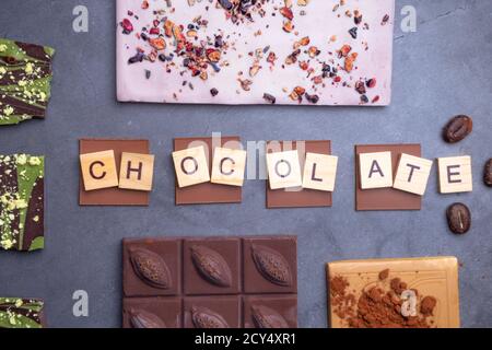 Mélange de morceaux de barres de chocolat en noir, lait, noix et chocolat blanc, avec haricots, poeder de cacao sur fond de béton gris. Mise au point sélective Banque D'Images