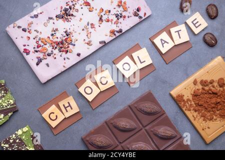 Mélange de morceaux de barres de chocolat en noir, lait, noix et chocolat blanc, avec haricots, poeder de cacao sur fond de béton gris. Mise au point sélective Banque D'Images
