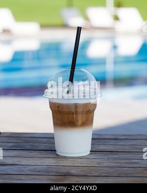 Latte froide dans un verre en plastique sur le fond d'une piscine extérieure dans la nature. Banque D'Images