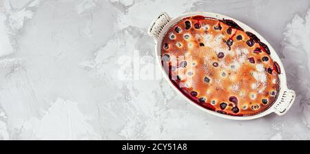 Tarte aux cerises à la clafoutis maison - dessert français traditionnel dans un plat de cuisson blanc isolé sur un fond gris avec espace copie, vue du dessus Banque D'Images