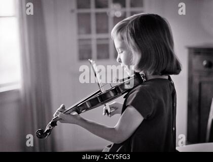 ANNÉES 1960 JOUER DU VIOLON CHARMANTE PETITE JEUNE FILLE BLONDE PRATIQUANT DES LEÇONS SUR UN INSTRUMENT DE TROIS QUARTS DANS LE SALON À LA MAISON - M7568 HAR001 HARS COPIER ESPACE DEMI-LONGUEUR CHAÎNES DE PRATIQUE B&W ARTS DE LA SCÈNE TEMPTATION RÊVES LEÇONS TAILLE LOISIRS À L'ON VIBREUR VIOLONS INSTRUMENT DE MUSIQUE CONCEPTUEL CHARMANT CROISSANCE JEUNES JEUNES NOIR ET L'ETHNIE BLANCHE DE RACE BLANCHE HAR001 PRATIQUE À L'ANCIENNE Banque D'Images