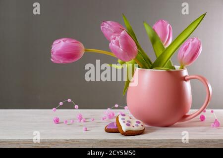 Bouquet de tulipes sur fond gris. Tulipes dans une tasse rose et deux biscuits au pain d'épice sur une table blanche Banque D'Images