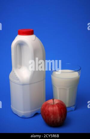 Carafe à lait étanche d'un gallon avec bouchon rouge, plein de lait en verre et pomme rouge sur fond bleu Banque D'Images