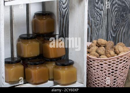 Confiture de fruits en pots. Se tient dans une caisse en bois peinte en blanc. À côté, il y a un panier de noix. Banque D'Images