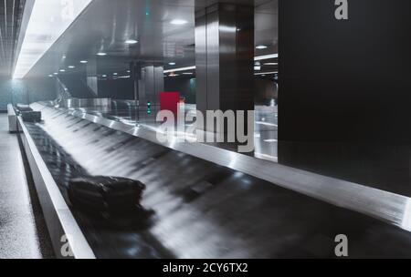 Une zone de récupération des bagages dans un hall sombre d'un zone d'arrivée à l'aéroport avec un convoyeur en mouvement et flou ceinture avec plusieurs sacs à bagages sur son pourtour Banque D'Images