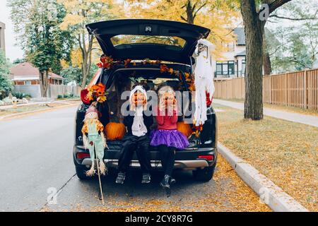 Trick ou tronc. Enfants célébrant Halloween dans le coffre de la voiture. Garçon et fille avec des citrouilles rouges célébrant les fêtes traditionnelles d'octobre en plein air. Social Banque D'Images