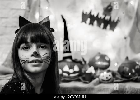 Enthousiaste à propos de Halloween. Photo en noir et blanc d'une jeune fille adorable en costume de chat noir et citrouille sculptée sur fond Banque D'Images