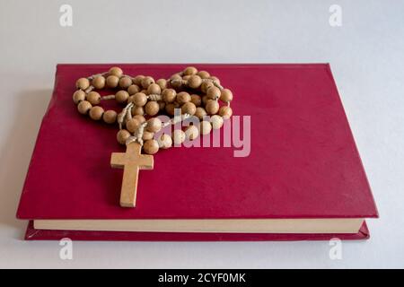 Petit livre de prière en cuir rose couverture couchée avec les extrémités des pages en avant avec rosaire catholique en bois avec croix sur elle pliée en forme de coeur. Banque D'Images