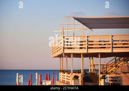 Plage avant l'ouverture, chaises longues et parasols pliés, tables vides dans un café au bord de la mer. Banque D'Images