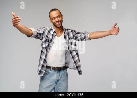 Sympathique homme afro-américain portant un t-shirt avec un sourire crasseux montrant des câlins geste sur fond gris Banque D'Images