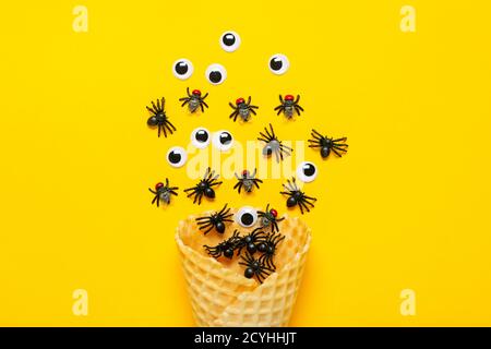 Araignées et mouches noires, yeux gogly rampent hors de glace cône sur fond jaune vue du dessus Flat Lay Happy Halloween Creative concept carte de vacances Banque D'Images