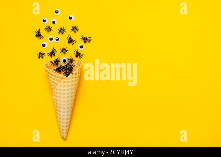 Araignées et mouches noires, yeux gogly rampent hors de glace cône sur fond jaune vue du dessus Flat Lay Happy Halloween Creative concept carte de vacances Banque D'Images