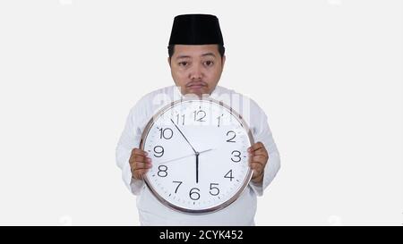 musulman asiatique avec un excès de poids debout et tenant une grande horloge en attendant la pause jeûne. islam fat boy ne peut pas attendre la pause musulmane jeûne conc Banque D'Images