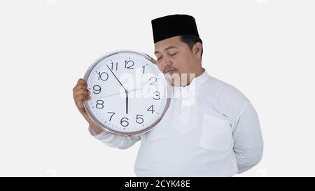 musulman asiatique avec un excès de poids debout et tenant une grande horloge en attendant la pause jeûne. islam fat boy ne peut pas attendre la pause musulmane jeûne conc Banque D'Images