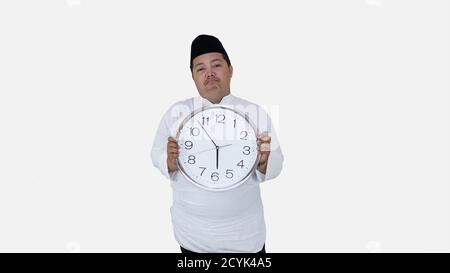 musulman asiatique avec un excès de poids debout et tenant une grande horloge en attendant la pause jeûne. islam fat boy ne peut pas attendre la pause musulmane jeûne conc Banque D'Images