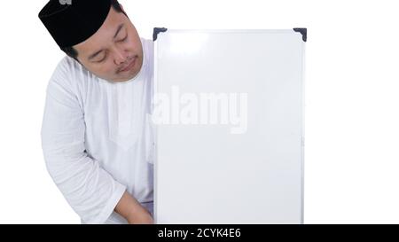 souriant musulman asiatique avec un surpoids debout et tenant le tableau blanc présentant un espace coppy. Banque D'Images