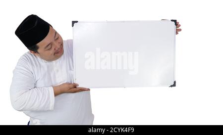 souriant musulman asiatique avec un surpoids debout et tenant le tableau blanc présentant un espace coppy. Banque D'Images