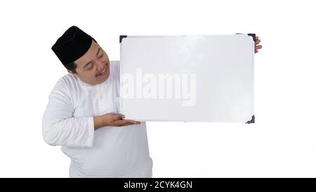 souriant musulman asiatique avec un surpoids debout et tenant le tableau blanc présentant un espace coppy. Banque D'Images