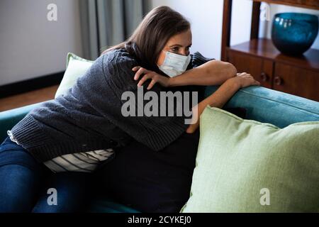 Femme âgée portant un masque facial assise sur un canapé à la maison Banque D'Images