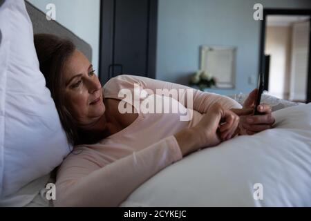 Femme âgée utilisant un smartphone dans le lit à la maison Banque D'Images