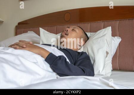 Homme asiatique fatigué dormant avec la bouche ouverte après le travail un lit confortable dans sa chambre à la maison Banque D'Images