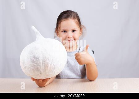 l'enfant montre les pouces et tient une maison Serviettes en potiron et décorations en papier pour Halloween Banque D'Images